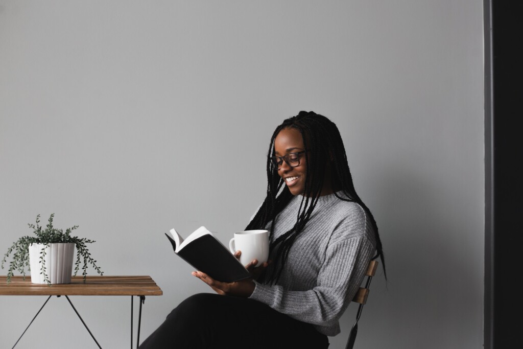 woman sitting in a chair with a small table, reading her Bible and drinking coffee